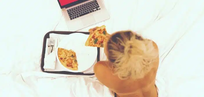 woman sitting on bed while eating pizza